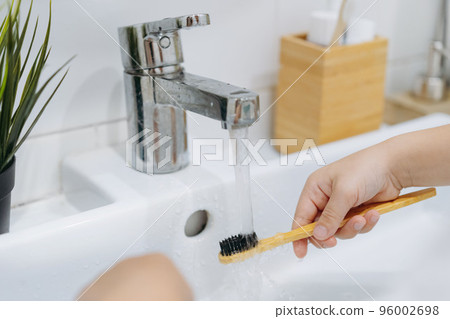 child is rinsing bamboo tooth brus with water running from sink tap 96002698
