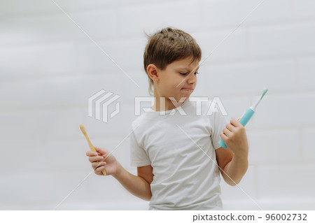 cute 8 years old boy holding bamboo and electric tooth brush making choice cute 8 years old boy holding bamboo and electric tooth brush making choice 96002732