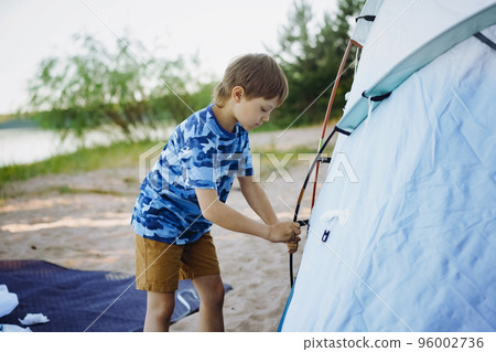cute little caucasian boy helping to put up a tent. Family camping concept cute little caucasian boy helping to put up a tent. Family camping concept 96002736