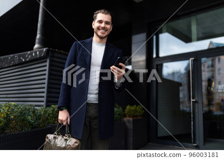 young businessman with a wide smile on his face with a mobile phone in his hands and a briefcase for 96003181