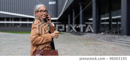 adult successful business woman walks into an office building talking on a mobile phone with a cup adult successful business woman walks into an office building talking on a mobile phone with a cup 96003195