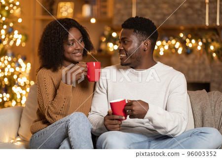 Happy millennial african american couple with cups of favorite hot drink enjoy holiday together on sofa 96003352