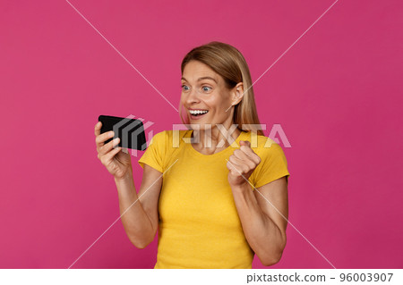 Surprised happy adult european lady with smartphone rejoices to victory, makes success gesture with hand 96003907