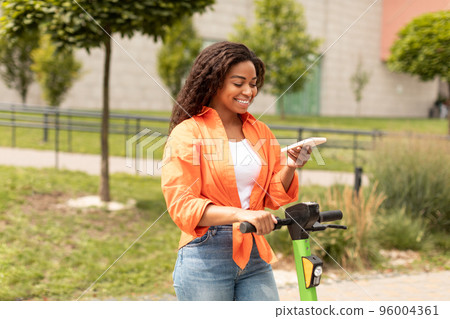Cheerful millennial black woman on electric scooter typing on smartphone, enjoy walk Cheerful millennial black woman on electric scooter typing on smartphone, enjoy walk 96004361