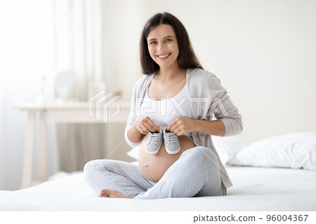 Happy pregnant woman holding baby shoes on her big tummy 96004367