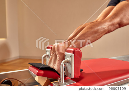 Fit man doing a lunge stretch yoga pilates exercise to strengthen and tone his muscles using a reformer in a gym 96005109