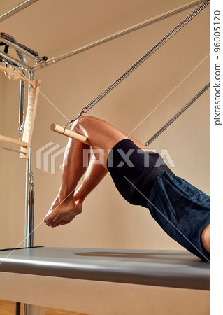 Fit man doing a lunge stretch yoga pilates exercise to strengthen and tone his muscles using a reformer in a gym Fit man doing a lunge stretch yoga pilates exercise to strengthen and tone his muscles using a reformer in a gym 96005120