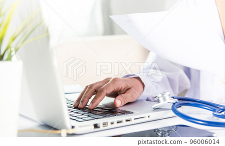 Doctor or nurse woman in uniform with stethoscope working she typing information of patient prescription from paperwork medical history form into laptop computer for recording document data report 96006014
