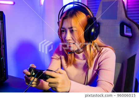 Woman wear gaming headphones playing live stream esports games console at home, Gamer using joystick controller for virtual tournament plays online video game with computer neon lights, Esport concept 96006015