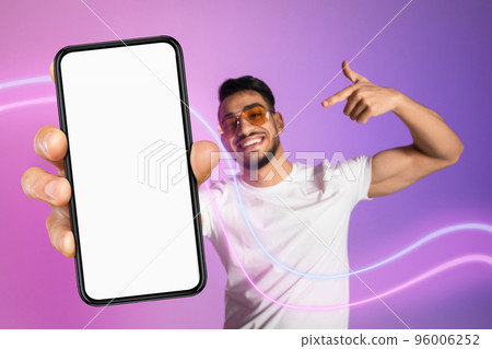 Cheerful arab guy in sunglasses pointing at modern cell phone Cheerful arab guy in sunglasses pointing at modern cell phone 96006252