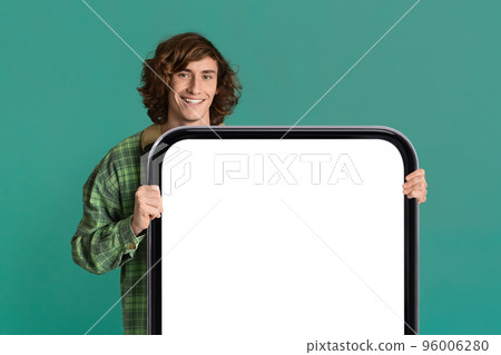 Smiling Millenial Hipster Guy Standing Behind Big Blank Smartphone With White Screen Smiling Millenial Hipster Guy Standing Behind Big Blank Smartphone With White Screen 96006280