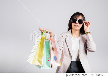 Happy woman with glasses confident shopper smiling holding online shopping bags colorful multicolor, Portrait excited Asian young female purchase studio shot isolated on white background, fashion sale 96008422