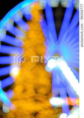 Ferris wheel decorated with blue illumination and a large Christmas tree decorated with yellow illumination on a black background at night. Beautiful New Year and Christmas holiday blurred background Ferris wheel decorated with blue illumination and a large Christmas tree decorated with yellow illumination on a black background at night. Beautiful New Year and Christmas holiday blurred background 96008777