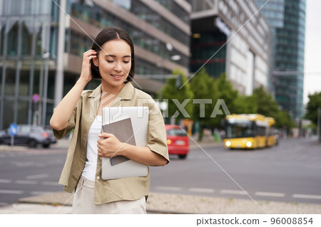 Portrait of beautiful asian woman standing on street with laptop and notebook, going to university or work, commute route Portrait of beautiful asian woman standing on street with laptop and notebook, going to university or work, commute route 96008854