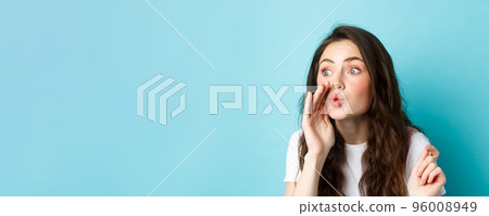 Cute glamour gossip girl spreading rumours, whispering news to someone, standing voer blue background 96008949