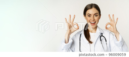 Happy beautiful woman doctor, showing okay, ok excellent sign, smiling amazed, approve smth, praise, standing in white lab coat over white background Happy beautiful woman doctor, showing okay, ok excellent sign, smiling amazed, approve smth, praise, standing in white lab coat over white background 96009059