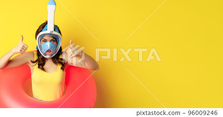 Funny happy woman in swimming ring, wearing snorkling mask for diving, showing thumbs up, good approval gesture, posing against yellow background 96009246