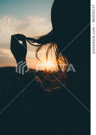 Silhouette photo of a woman standing in nature at sunset 96009337