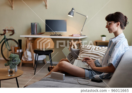 Young woman using laptop and relaxing on sofa Young woman using laptop and relaxing on sofa 96011665