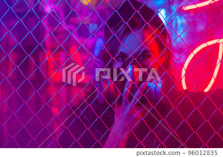 Caucasian woman in a gas mask behind a fence in a neon studio. Caucasian woman in a gas mask behind a fence in a neon studio. 96012835