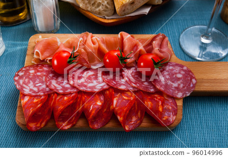 Spanish tasty meal slicing sausages and ham with tomatoes at wooden desk Spanish tasty meal slicing sausages and ham with tomatoes at wooden desk 96014996