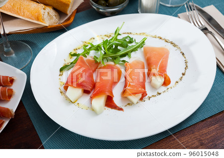 Spanish dish - rolls of iberian jamon stuffed with melon served with arugula Spanish dish - rolls of iberian jamon stuffed with melon served with arugula 96015048