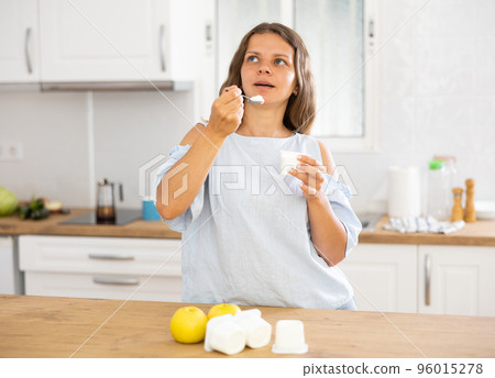 Young woman eating tasty yogurt in kitchen Young woman eating tasty yogurt in kitchen 96015278
