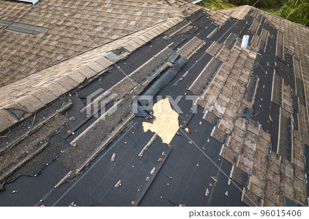 Wind damaged house roof with missing asphalt shingles after hurricane Ian in Florida. Repair of home rooftop concept Wind damaged house roof with missing asphalt shingles after hurricane Ian in Florida. Repair of home rooftop concept 96015406