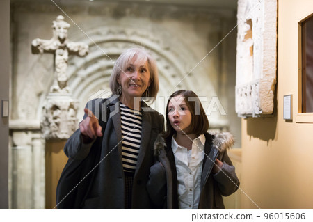 Aged female tutor with preteen girl exploring showpieces in museum Aged female tutor with preteen girl exploring showpieces in museum 96015606