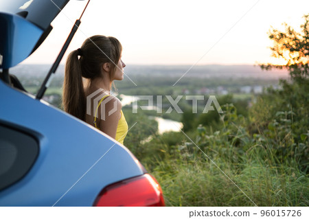 Carefree woman driver in yellow summer dress enjoying warm evening near her car. Travel and vacation concept. Carefree woman driver in yellow summer dress enjoying warm evening near her car. Travel and vacation concept. 96015726