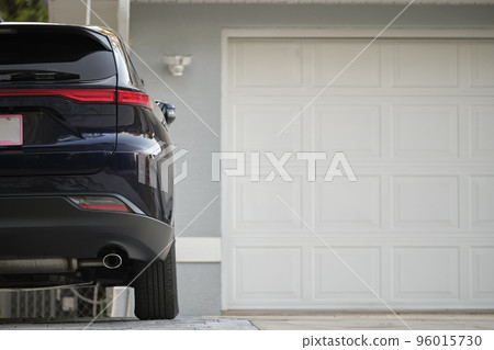 Car parked in front of wide garage double door on concrete driveway of new modern american house Car parked in front of wide garage double door on concrete driveway of new modern american house 96015730