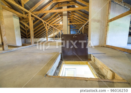 Attic of a building with wooden beams of a roof structure and a fire exit door in floor. 96016250