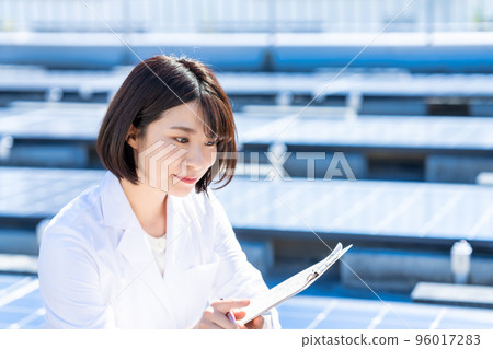 A woman in a white coat measuring a solar panel in a laboratory A woman in a white coat measuring a solar panel in a laboratory 96017283