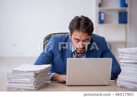 Young male employee and too much work in the office Young male employee and too much work in the office 96017905