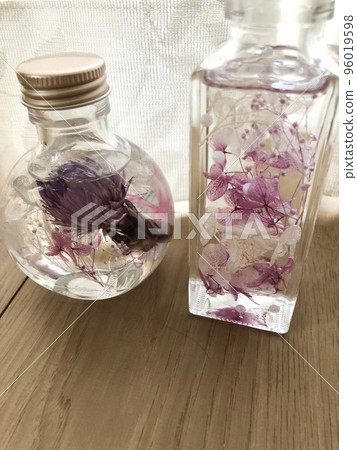 A picture taken from the front of two pink herbariums in a round glass bottle and a vertically long glass bottle. 96019598