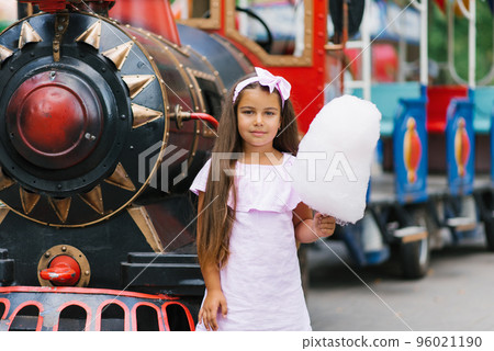 Child girl in an amusement park in the summer eats cotton candy and smiles happily. The concept of summer holidays and school holidays 96021190