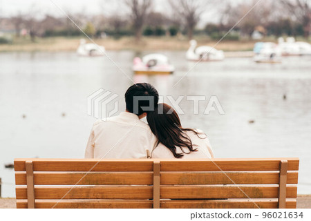 一對夫婦從長凳上依偎著,看著天鵝船漂浮的池塘的後視圖 一對夫婦從長凳上依偎著,看著天鵝船漂浮的池塘的後視圖 96021634