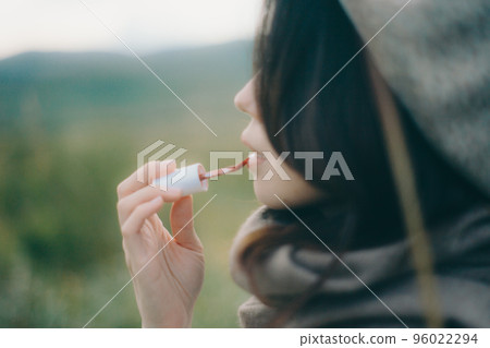 Photo of a woman standing in nature and applying gloss Photo of a woman standing in nature and applying gloss 96022294