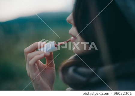 Photo of a woman standing in nature and applying gloss Photo of a woman standing in nature and applying gloss 96022301