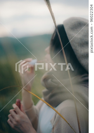 Photo of a woman standing in nature and applying gloss Photo of a woman standing in nature and applying gloss 96022304
