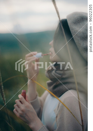 Photo of a woman standing in nature and applying gloss 96022305