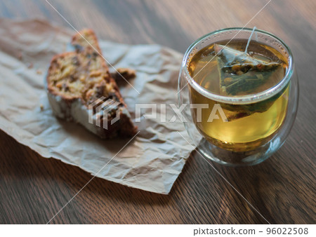 Herbal tea in glass and biscuit on craft paper. Cozy breakfast. Tea bag in glass with cake. Hot drink and dessert. Fresh bakery and tea in cafe.  96022508