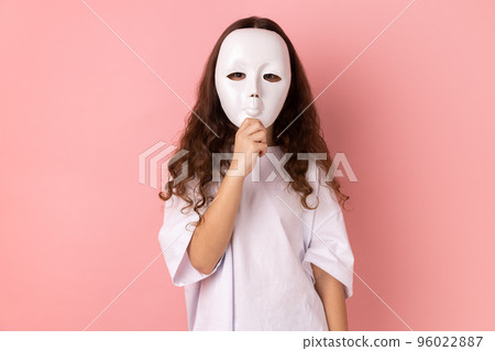 Portrait of unknown anonymous little girl wearing white T-shirt covering his face with white mask, hiding personality, conspiracy and privacy, secrets. Indoor studio shot isolated on pink background. 96022887