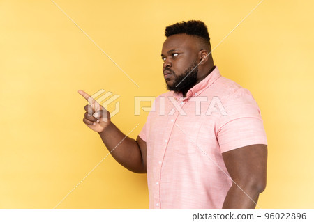 I told you. Side view of man wearing pink shirt pointing finger and looking ahead with dissatisfied suspicious expression, warning about troubles. Indoor studio shot isolated on yellow background. I told you. Side view of man wearing pink shirt pointing finger and looking ahead with dissatisfied suspicious expression, warning about troubles. Indoor studio shot isolated on yellow background. 96022896