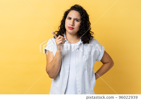 Portrait of serious strict woman with dark wavy hair pointing finger at camera and looking with dissatisfied suspicious expression. Indoor studio shot isolated on yellow background. 96022939