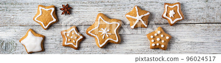 Border of Christmas gingerbreads in the shape of a star with patterns of glaze and spices on a white wooden background. 96024517