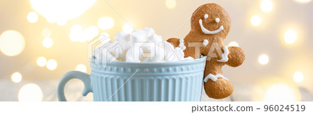 banner of a blue cup of winter hot drink with marshmallows and gingerbread man on a white wooden background with bokeh. banner of a blue cup of winter hot drink with marshmallows and gingerbread man on a white wooden background with bokeh. 96024519