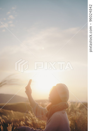 Photo of a woman listening to music in nature at sunset 96024842