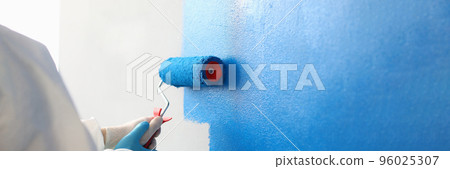 Painter with brush tool covered in blue colour painting wall Painter with brush tool covered in blue colour painting wall 96025307