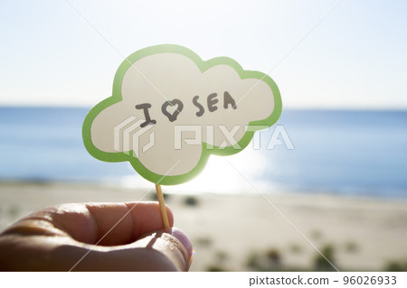 Stick with paper speech bubble with words I love sea on background blue sea sky sandy beach on sunny summer day. Text-balloons with text from letters. Concept symbol sign vacation travel tourism rest Stick with paper speech bubble with words I love sea on background blue sea sky sandy beach on sunny summer day. Text-balloons with text from letters. Concept symbol sign vacation travel tourism rest 96026933